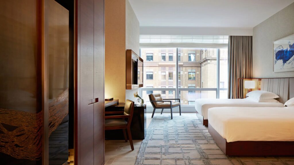 A hotel room with two beds at the park Hyatt New York with windows looking out to midtown manhattan. 