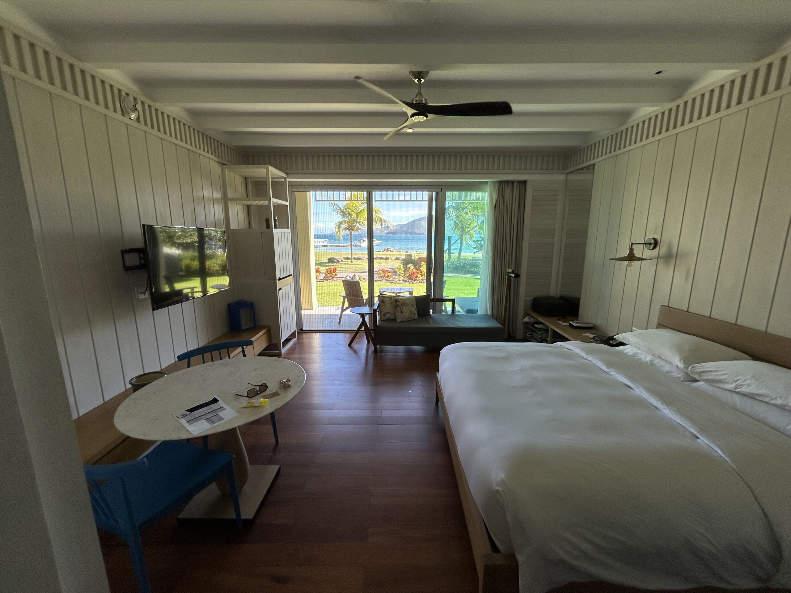 a king bed, small table, couch and wall-mounted TV in a hotel room with an ocean view.