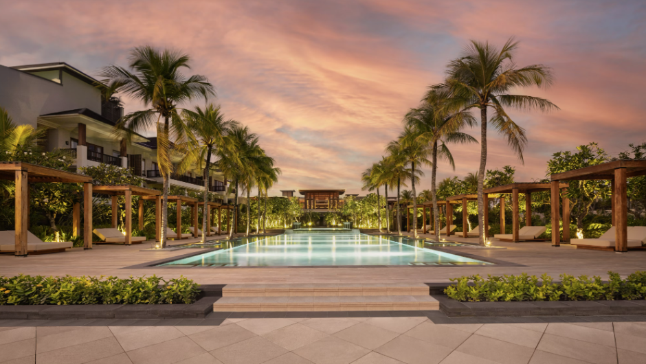 A hotel pool at sunset lined with daybeds and palm trees. 