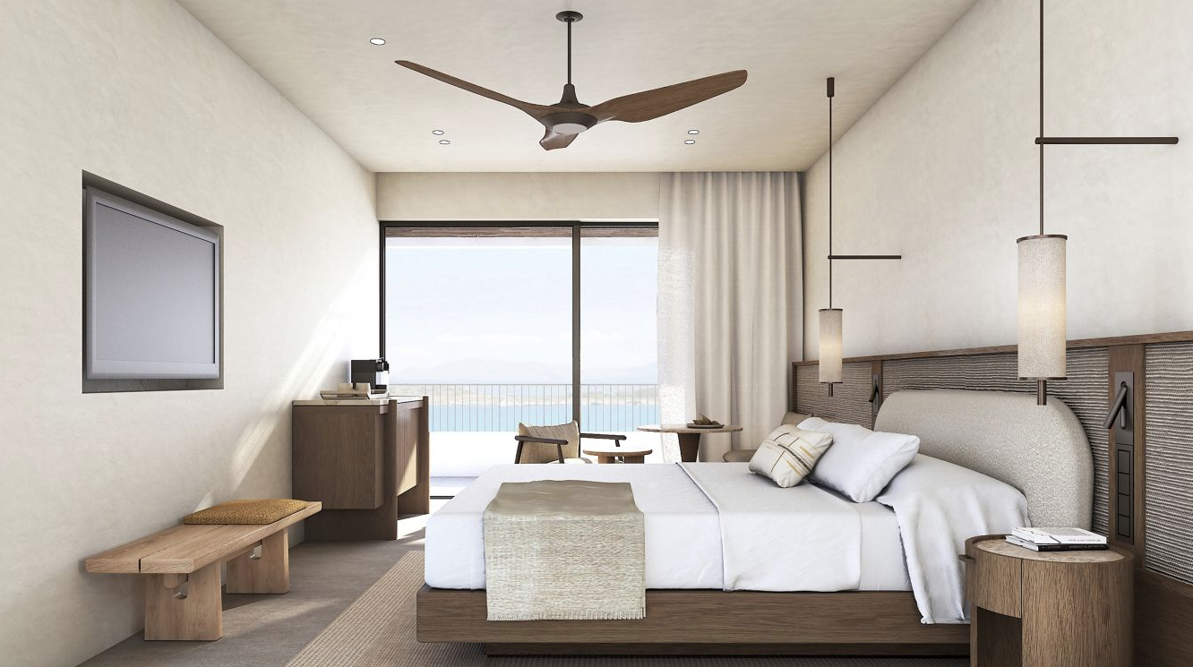 A hotel room with a large bed, white walls, a tv built into the wall and a balcony with a view of the ocean. 