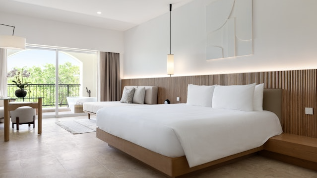 Kimpton Tres Rios bedroom with a large bed, small day bed and a desk with a balcony. 