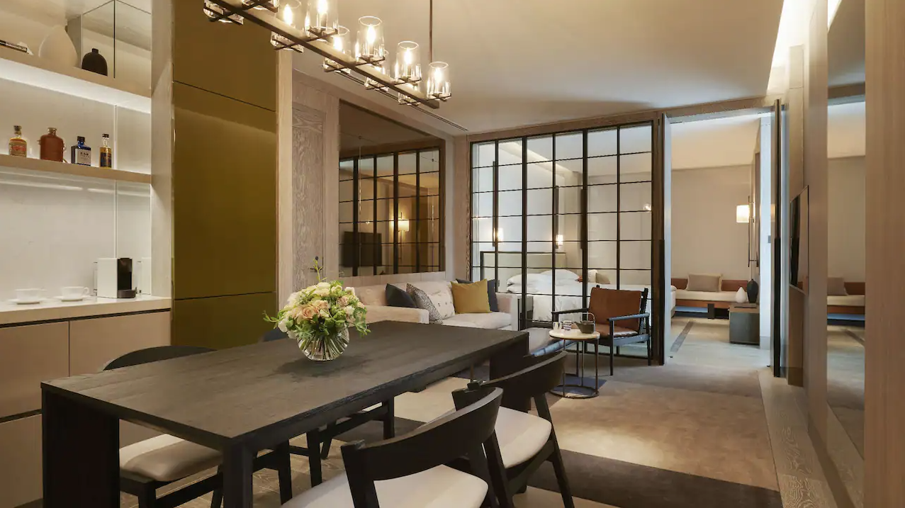 spacious hotel room with a full dining room table, couch, and a bedroom separated by a glass wall