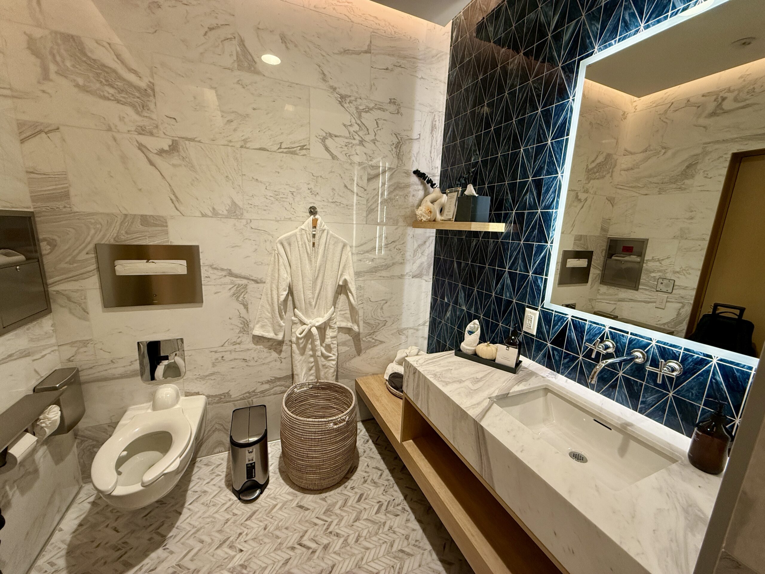 white marble and blue tile bathroom with toilet, sink and a bathrobe hanging on a wall hook