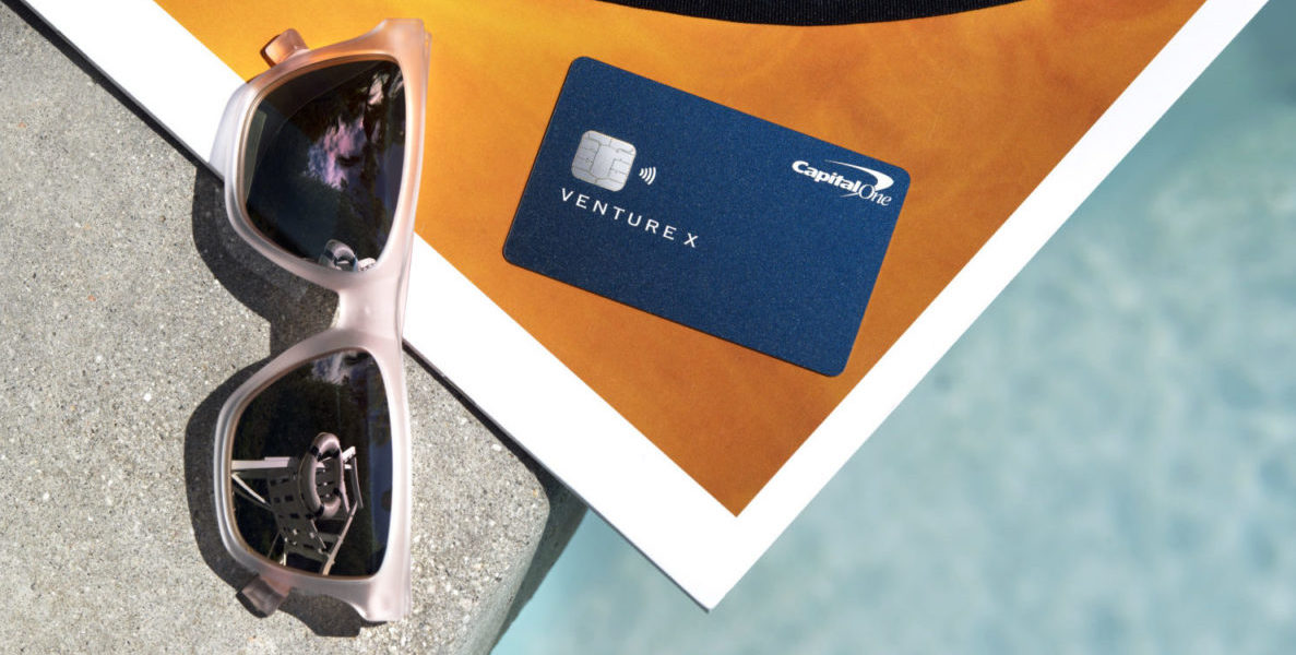 a capital one venture x card lying on top of a beach towel next to a pair of pink sunglasses