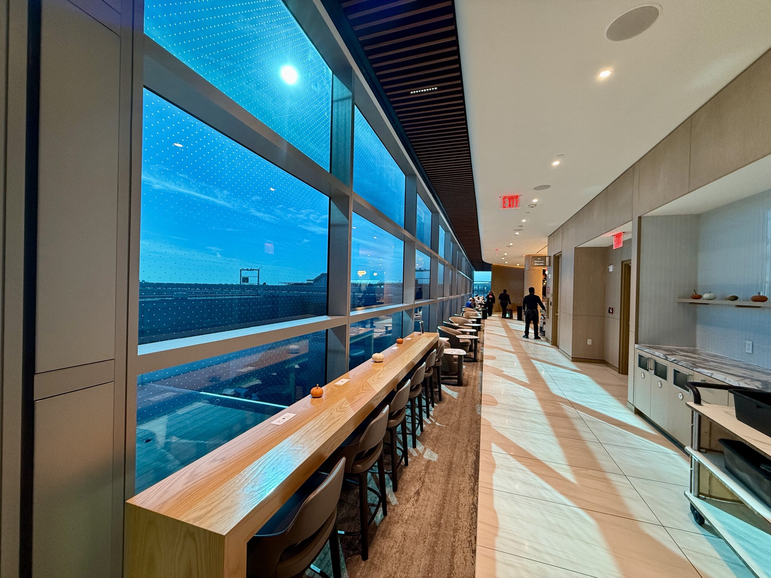 a long hallway with a long table and chairs looking out blue-tinted windows