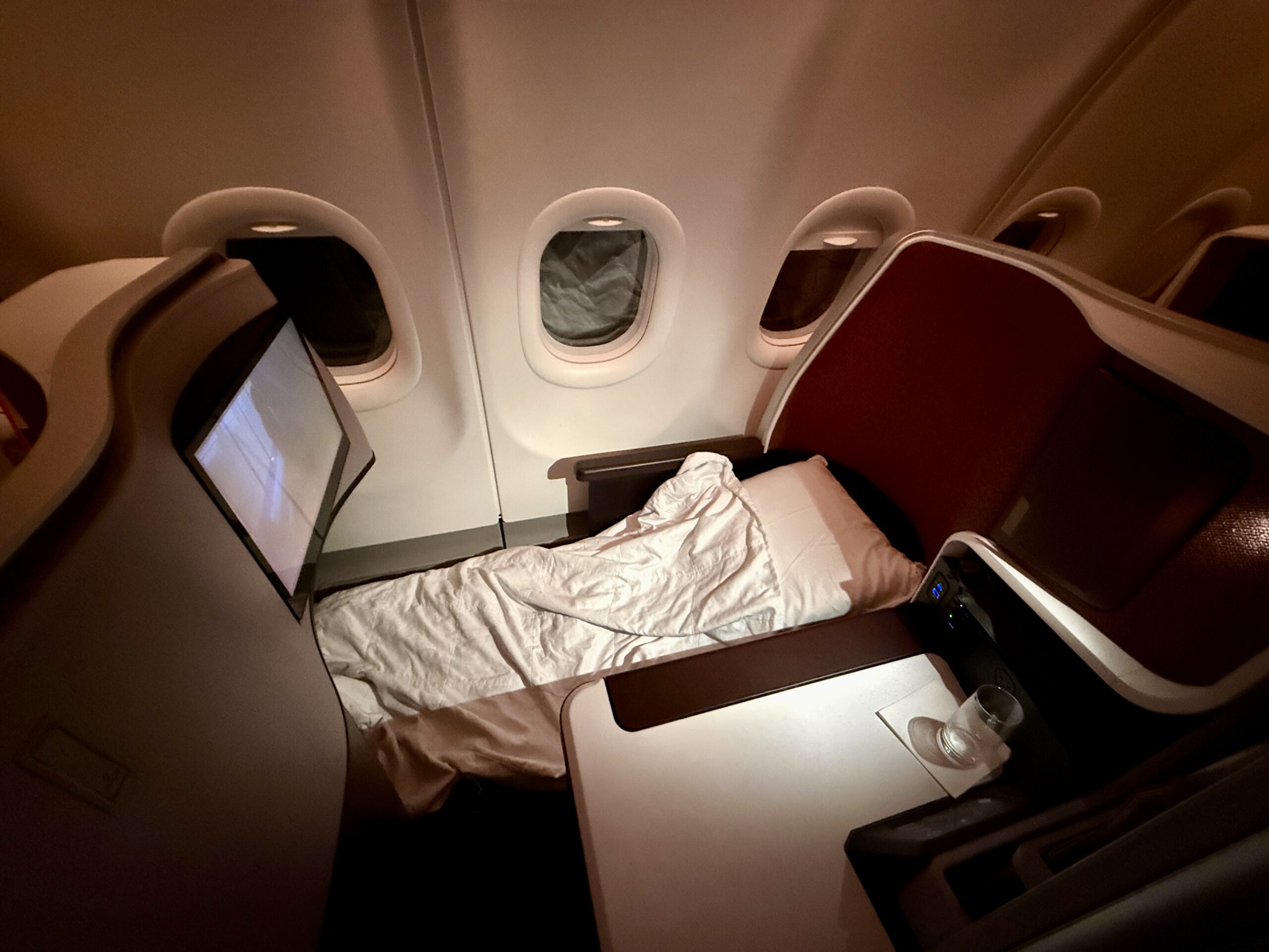 lie flat bed in a business class seat on a plane with a mattress pad, blanket and pillow.