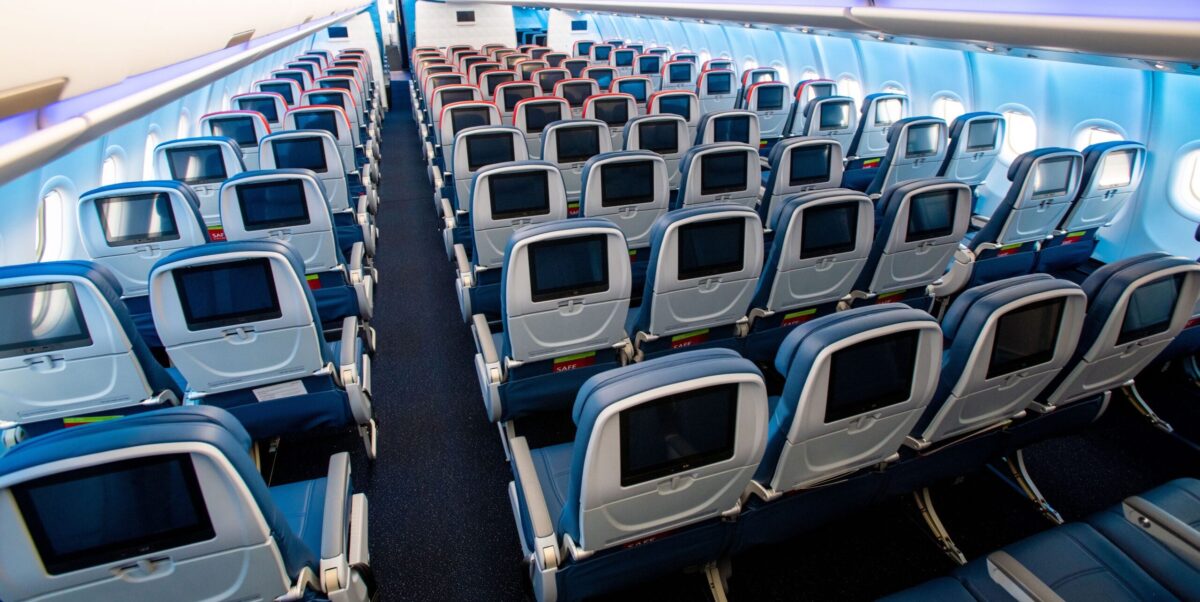 multiple rows of blue airplane seats with screens on a plane