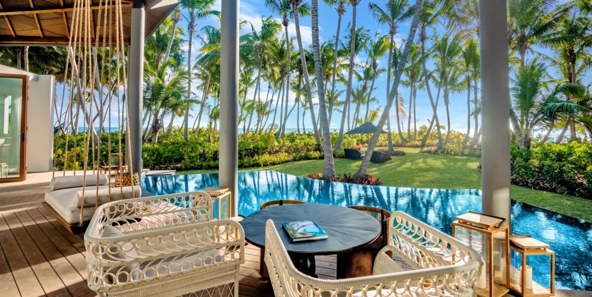 chairs sitting in front of a pool on a deck with palm trees and green grass in the background